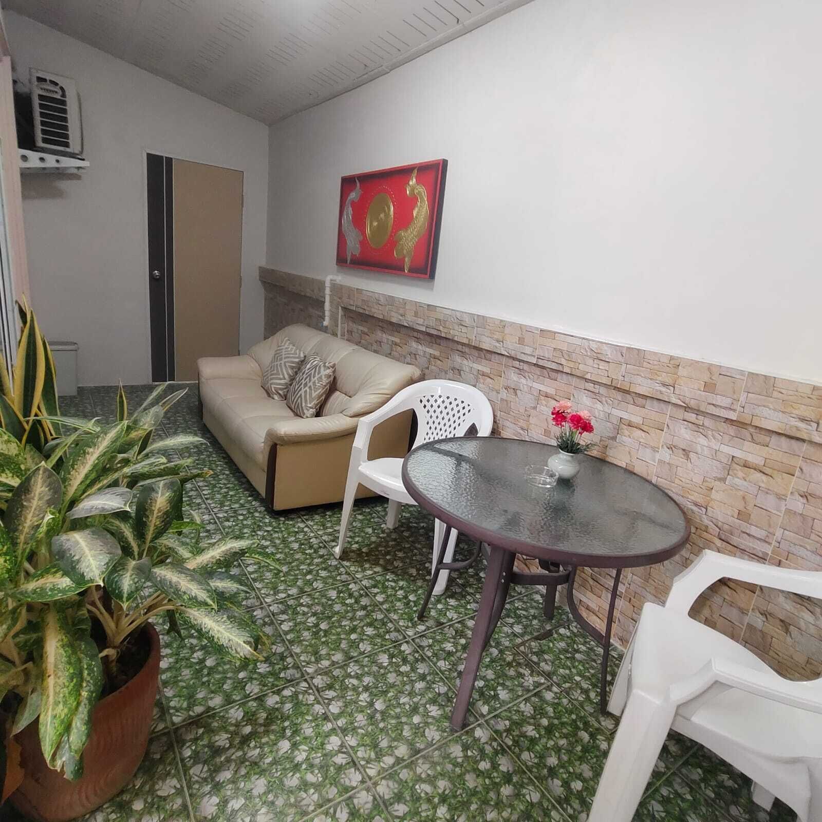 A small, furnished room with a sofa, a table, and potted plants.