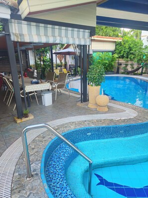 A pool area with a covered seating area, a dining table, and a pool with a tiled edge. -  2-bedroom luxurious house with swimming pool. (Tambon San Sai Noi)