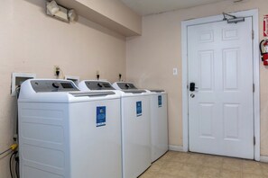 A laundry room with three front-loading washing machines and a white door. - Cozy 2-bedroom Hotel Suites in charming Steamboat Springs (Steamboat Springs)