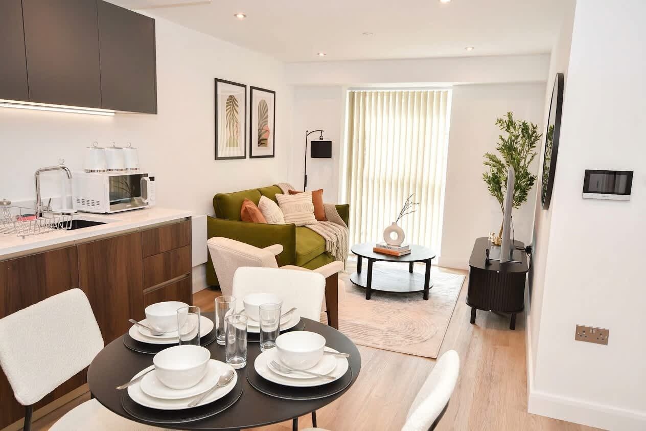A modern kitchen with a microwave, a dining table set with plates and glasses, a green sofa, and a small side table with a plant.