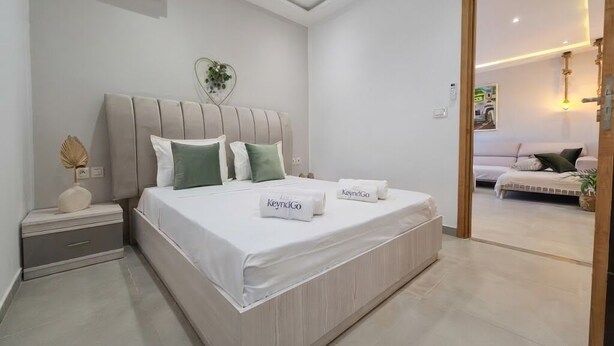 A modern bedroom with a large bed, bedside tables, and a view into another room. - Sandra 13 (Marsa)