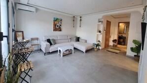 A modern living room with a sectional sofa, a coffee table, and a dining area with a wooden table and chairs. - Sandra 13 (Marsa)