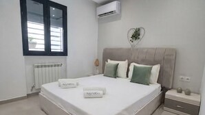 A bedroom with a bed, a bedside table, an air conditioning unit, a radiator, and a window with blinds. - Sandra 13 (Marsa)