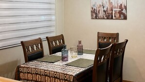 A dining area with a table set for four, a cityscape painting on the wall, and a ceiling light fixture. - Cozy and spacious home with parking (Los Angeles)