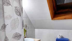 A bathroom with a white toilet, a sink with a wooden countertop, a blue bath mat, and a shower curtain with a leaf pattern. - Cozy and spacious home with parking (Los Angeles)