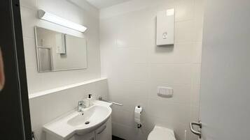 Un baño moderno con lavamanos blanco, espejo, inodoro y un calentador mural.