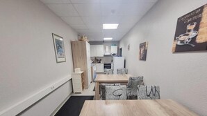 Um corredor estreito com uma mesa e cadeiras de madeira, uma cozinha compacta ao fundo e um quadro na parede.