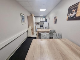 Un pasillo estrecho con una mesa y sillas de madera, una kitchenette al fondo y un cuadro en la pared.