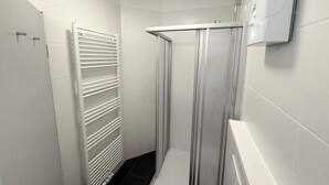 Um banheiro moderno com chuveiro sem barreiras, um radiador branco e um vaso sanitário branco.