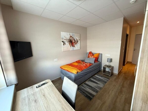 A modern bedroom with a bed, a desk, a chair, a TV, and a painting on the wall.