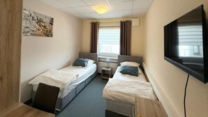 Quarto de hotel com duas camas de solteiro, uma escrivaninha, uma cadeira, uma televisão e uma janela com cortinas.
