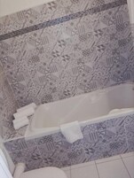 Un baño con bañera, baldosas estampadas y un inodoro.