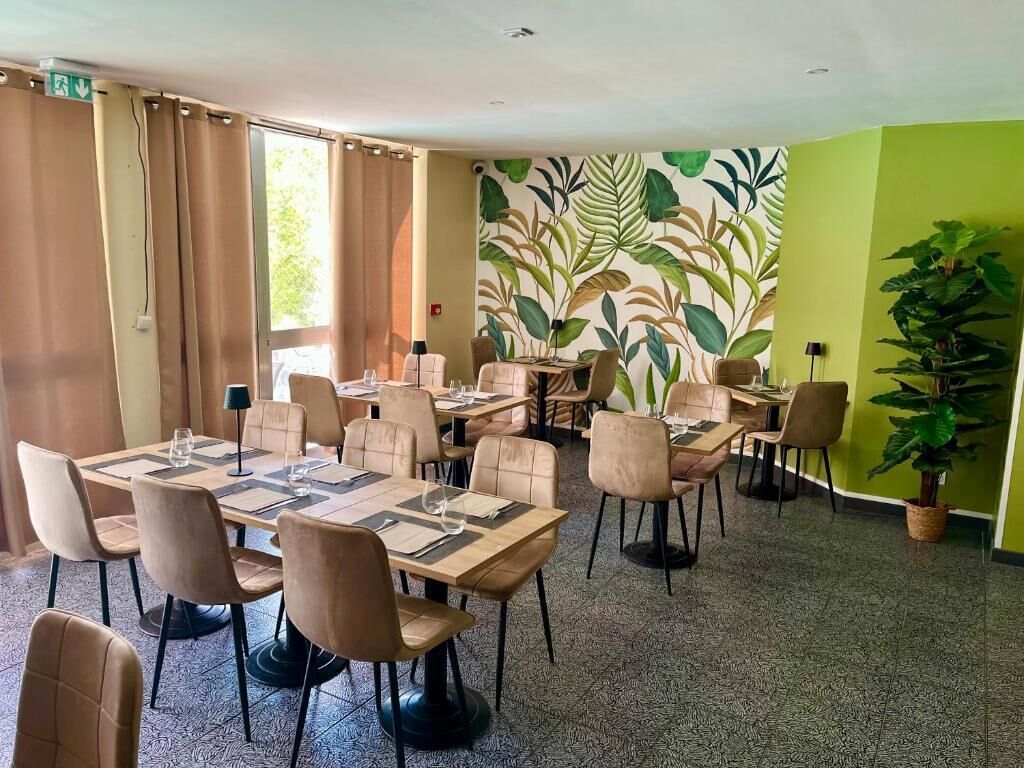 Un comedor con varias mesas y sillas, un muro con diseño y una planta en maceta.