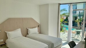 Een hotelkamer met twee bedden, een houten hoofdeinde, een eettafel en uitzicht op een buitenzwembad.