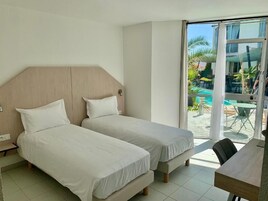 Habitación de hotel con dos camas, cabecero de madera, una mesa de comedor y vistas a una piscina al aire libre.