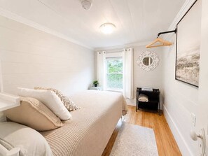 A bedroom with a bed, bedside table, and a window with curtains. - Hawkins House & Henry's Hideaway (Twillingate)