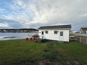 A small white building with a dock, red chairs, and a grassy area. - Hawkins House & Henry's Hideaway (Twillingate)
