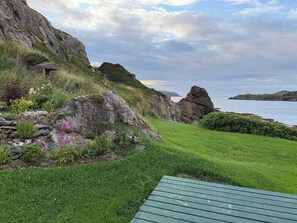 Eine Küstenlandschaft mit einer grünen Wiese, einem Felsen und Blick aufs Meer.