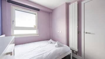 A bedroom with a single bed, a window with blinds, a radiator, and a door.