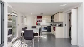 A modern kitchen with a dining area, featuring a central island, built-in appliances, and a view through the glass door.