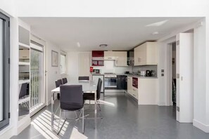 Cocina moderna con comedor, que incluye una isla central, electrodomésticos integrados y vistas a través de un ventanal.