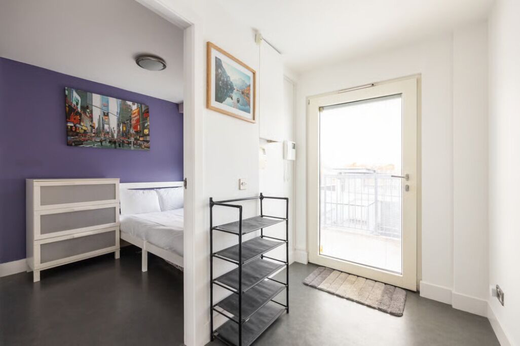 Een kamer met een bed, een witte dressoir, een metalen plank in het zwart, een deur met uitzicht en twee wanddecoraties.