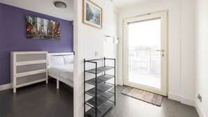 Ett rum med en säng, en vit byrå, en svart metallhylla, en dörr med utsikt och två tavlor som hänger på väggen.