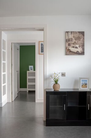 A hallway with a green door, a black console table with a vase of flowers, and a framed picture on the wall.