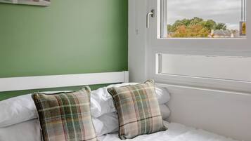 A bedroom with a bed, pillows, a window, and a view of the outside.