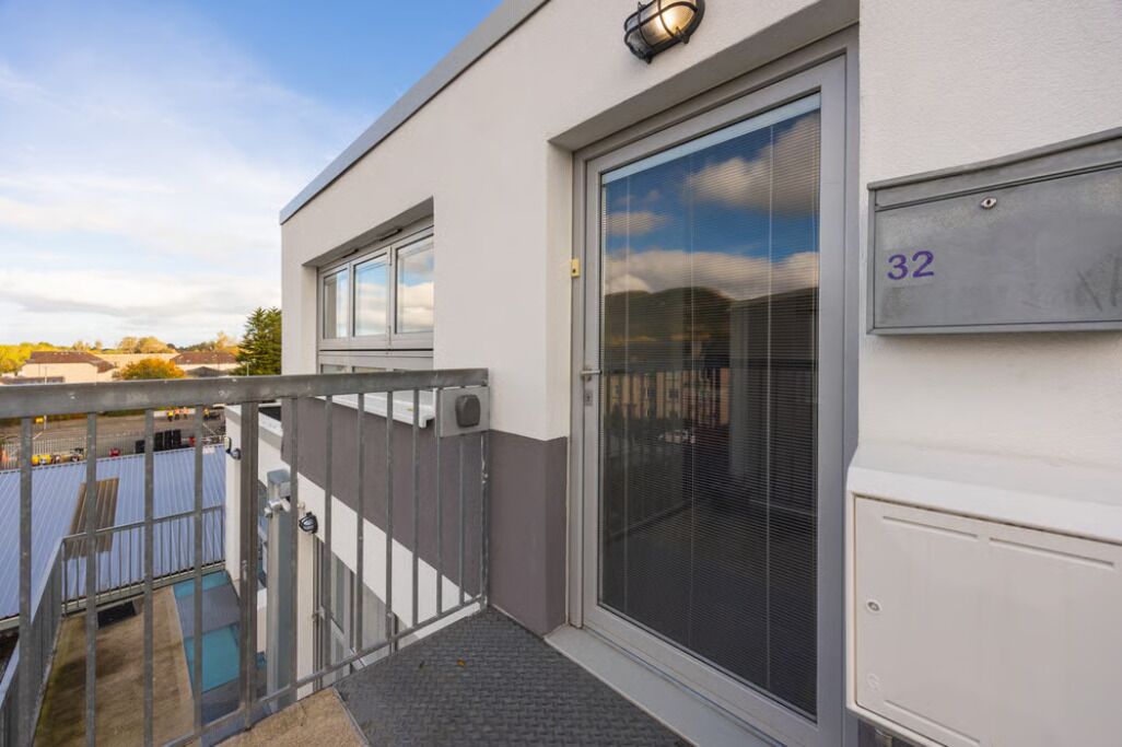 Een modern gebouw met een grote glazen schuindeur, een metalen hekwerk en een brievenbus met het nummer 32.