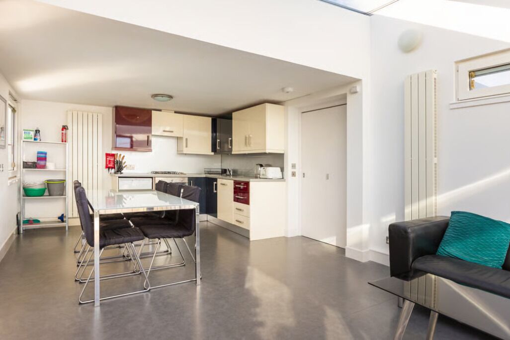 A modern kitchen with a dining area, a sofa, and a small window.