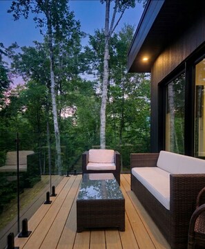 An outdoor seating area with wicker furniture and a glass table, surrounded by trees. - The NÖRA • Luxury Forest Retreat, Hot Tub • Sauna (La Conception)