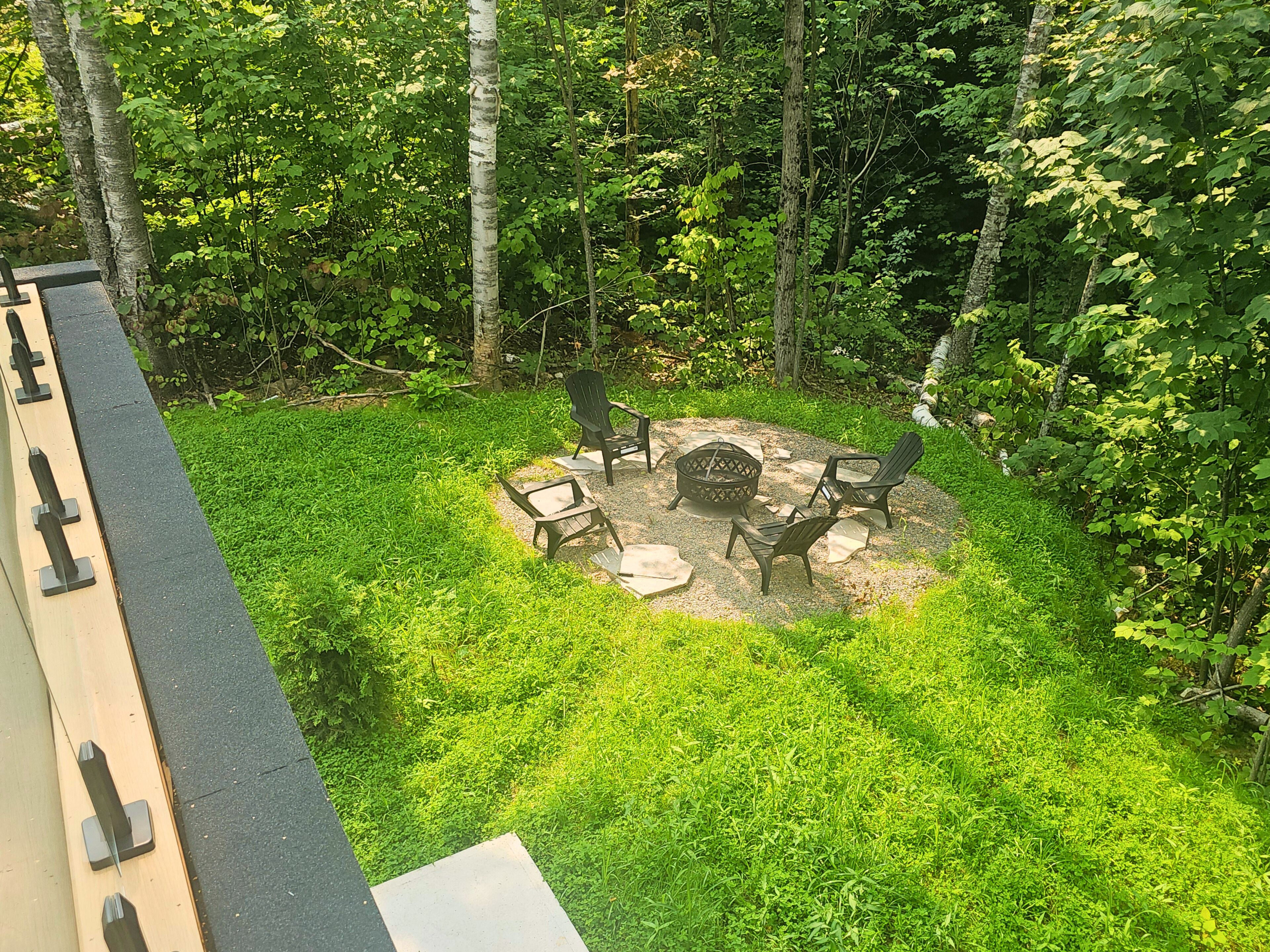A circular outdoor seating area with chairs and a fire pit surrounded by grass and trees.