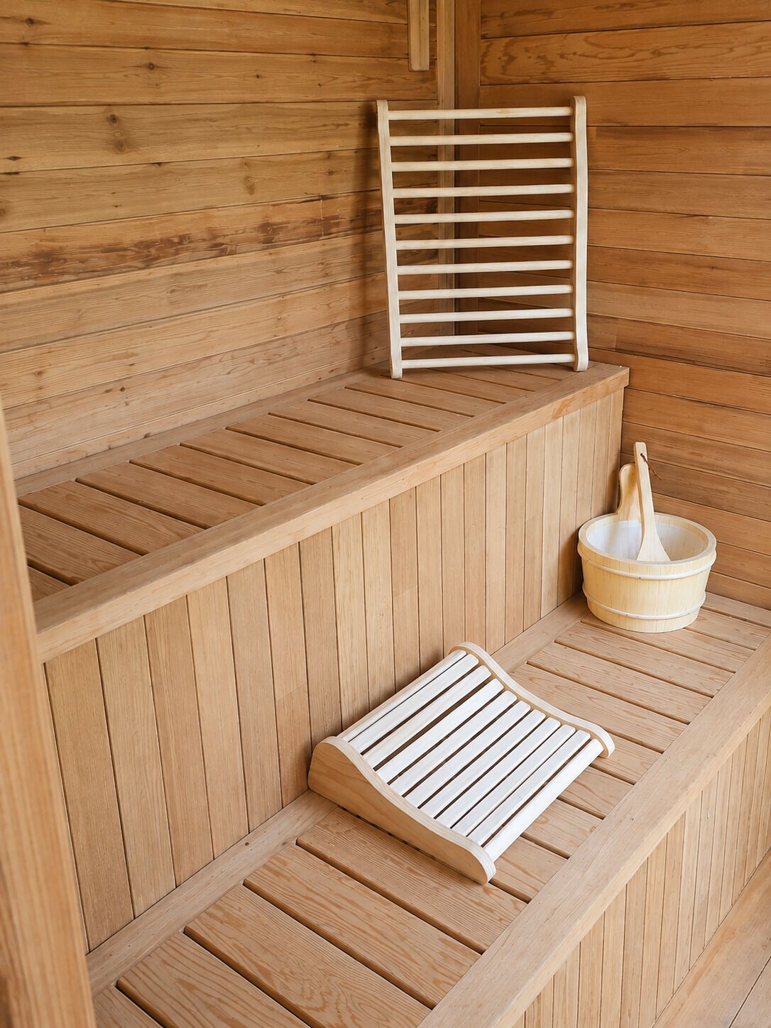 Eine Saunabank aus Holz mit Schlitzkonstruktion, eine Holzbank und ein Holzeimer.