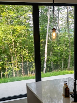 A room with a large window overlooking a forest, a marble countertop, and a hanging light fixture. - The NÖRA • Luxury Forest Retreat, Hot Tub • Sauna (La Conception)