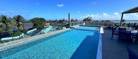 A swimming pool with a deck area, surrounded by palm trees and a view of the ocean.
