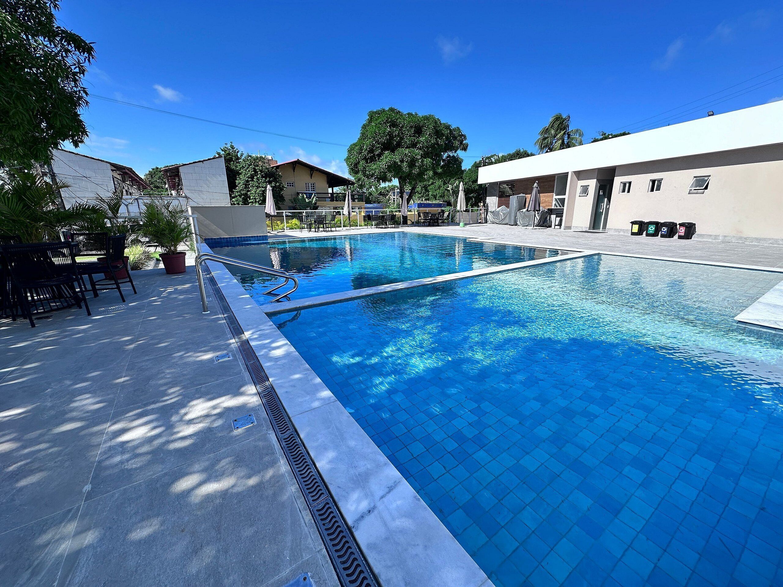 Ein Pool mit Fliesen umgeben von Gartenmöbeln und Blumentöpfen.