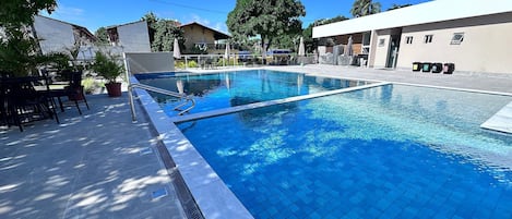 A swimming pool with a tiled deck, surrounded by outdoor furniture and potted plants.