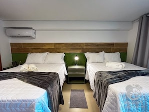 Ein Hotelzimmer mit zwei Betten, einem Nachttisch mit Lampe, einer Klimaanlage und einer Wand in Grünton.