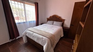 Ein Schlafzimmer mit einem Bett, einem Nachttisch, einem Holzschrank und einem Fenster mit Vorhängen.