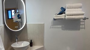 Ein Badezimmer mit weißem Waschbecken, einem Spiegel mit Beleuchtung, einem Handtuchhalter mit Handtüchern und einer Toilette.