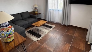 Ein Wohnzimmer mit Sofa, Couchtisch, Lampe, dekorativer Vase und einem an der Wand befestigten Fernseher.