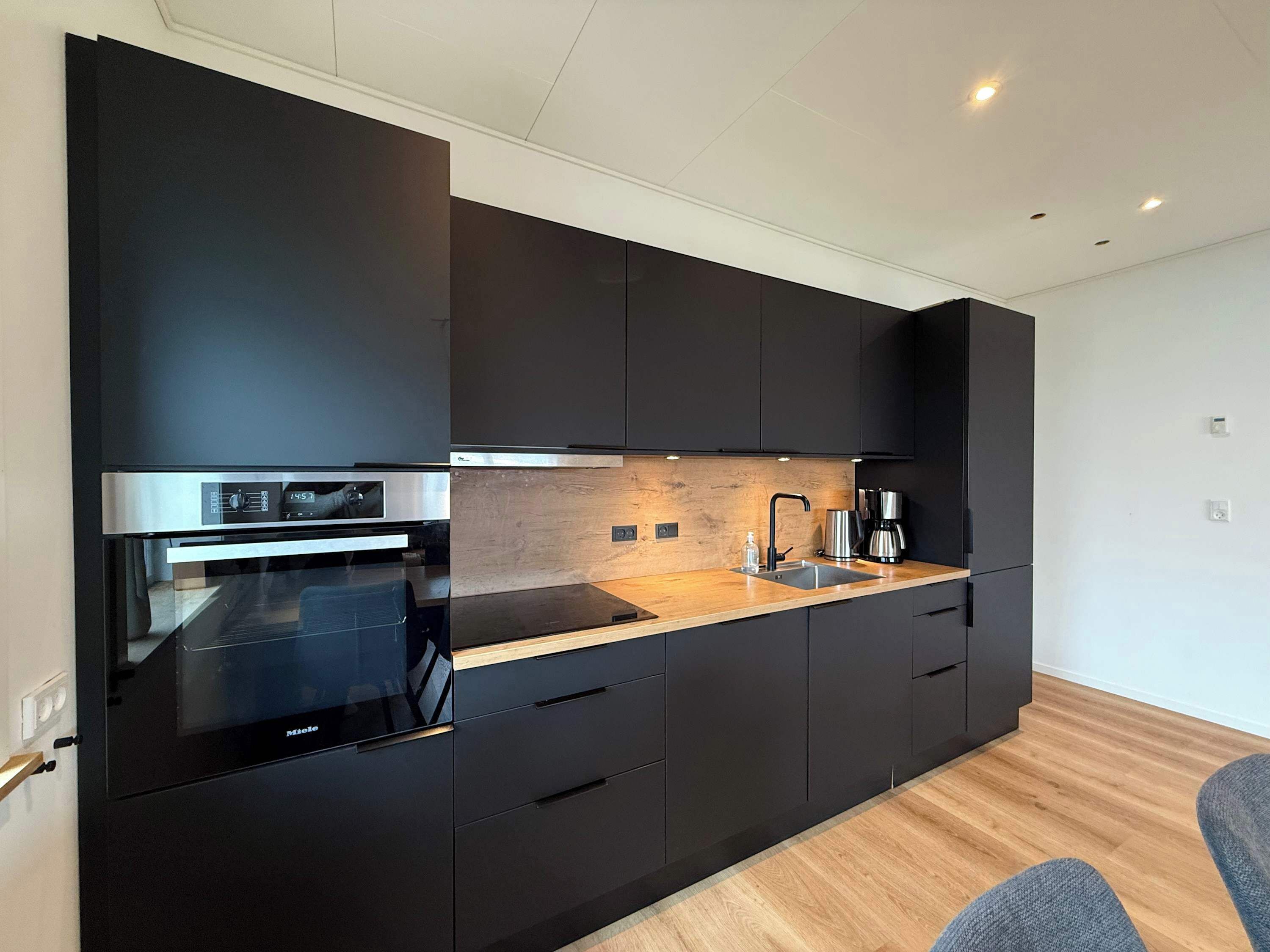 Eine moderne Küche mit schwarzen Schränken, einem Edelstahlbackofen, einer Holz Arbeitsplatte und einer Kaffeemaschine.