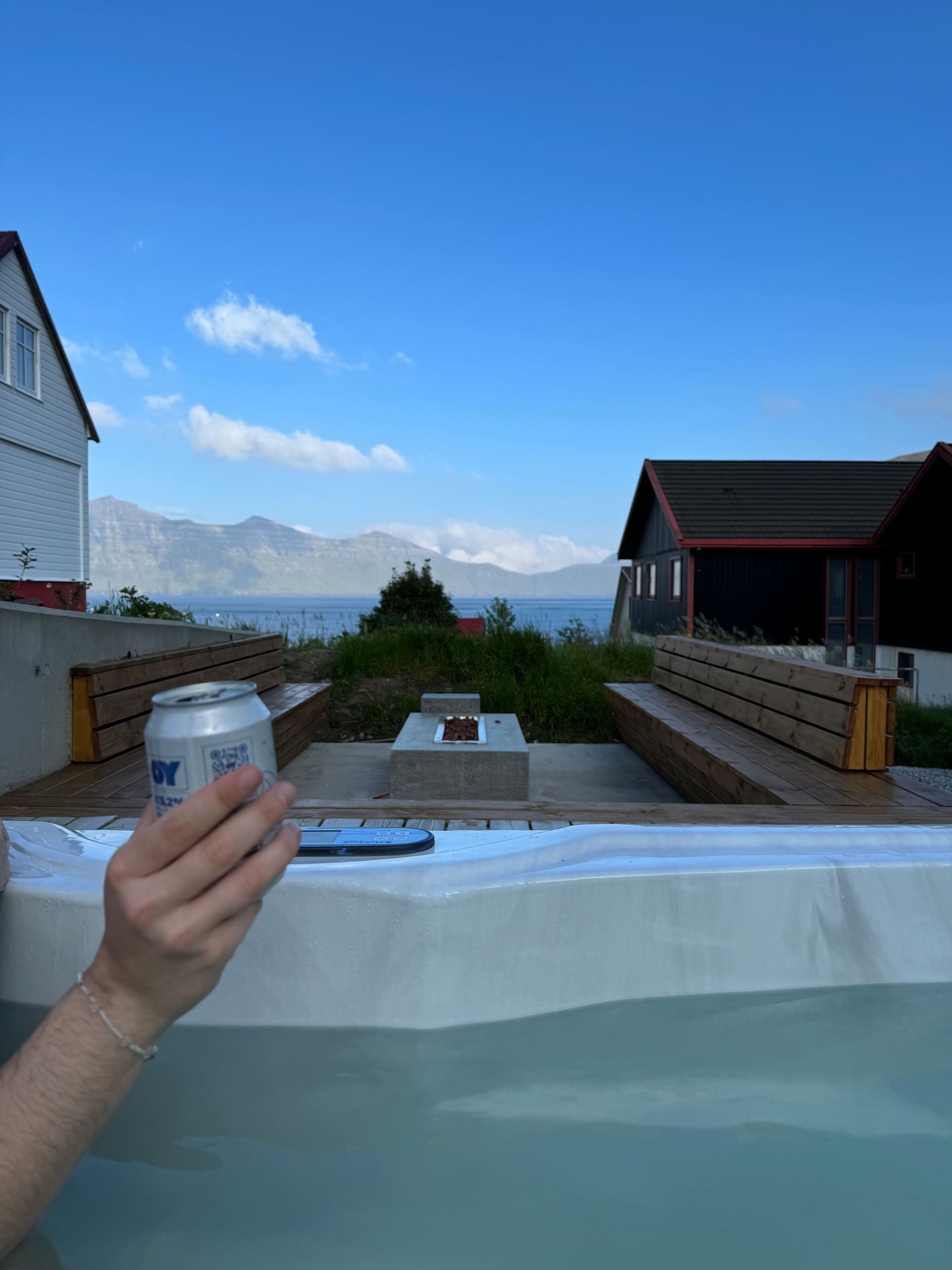 Una persona sosteniendo una lata, con vistas a una terraza y una vista de montañas y un cuerpo de agua.