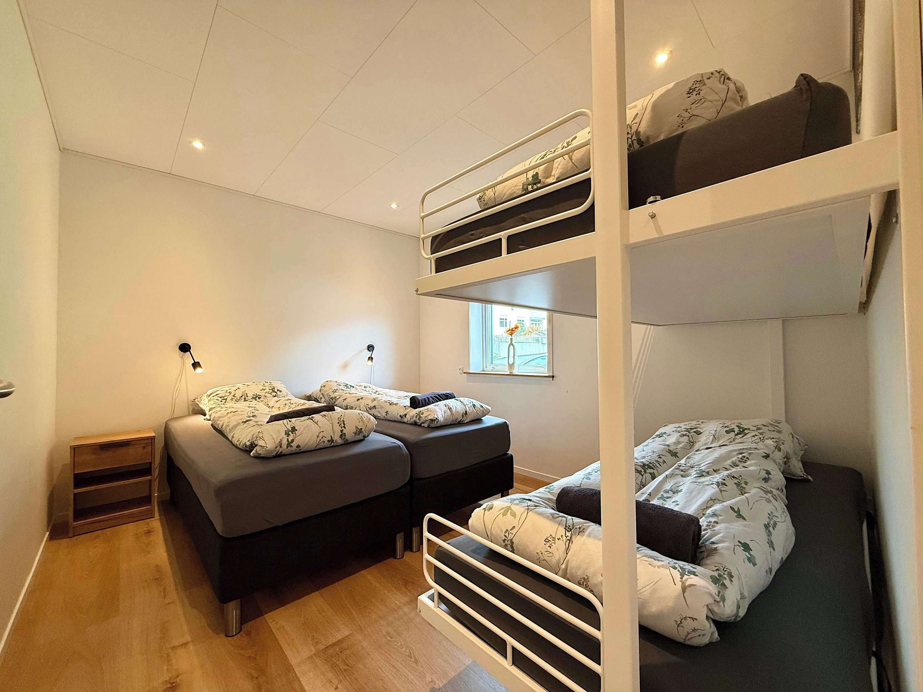 Ein Schlafraum mit Etagenbett, Fenster, Nachttisch und Lampe.