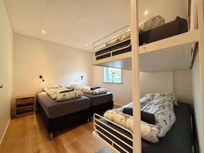 A bunk bed room with a window, a bedside table, and a lamp.
