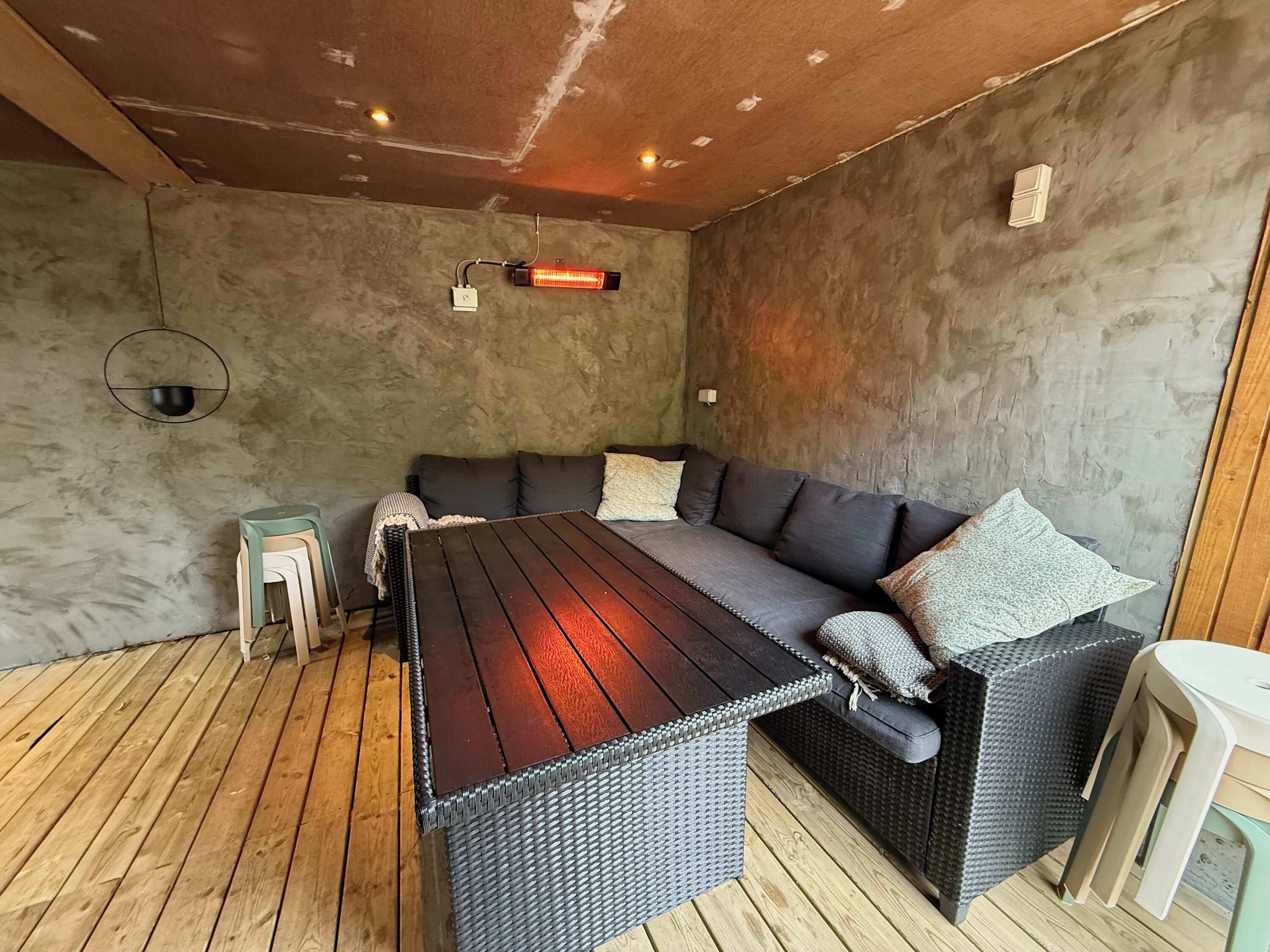Ein Zimmer mit einem dunkelgrauen Sofa, einem Holztisch und einem kleinen Hocker.