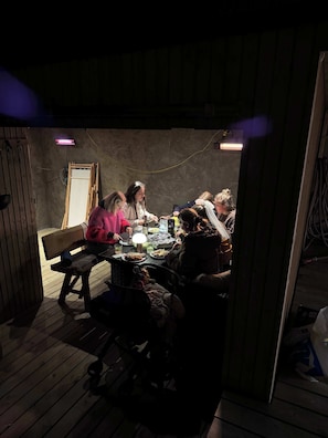 Un groupe de personnes est assis autour d’une table dans une pièce faiblement éclairée, aux murs en bois et où se trouve un banc.