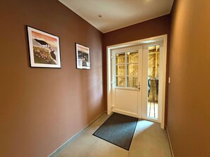 A hallway with a wooden door, a doormat, and two framed pictures on the wall.