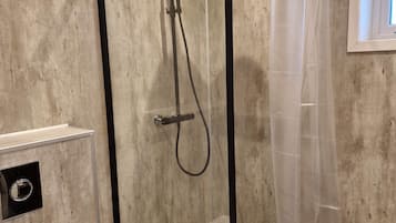 Suihkukaappi, jossa on lasiovi, wc ja ikkuna, josta tulee luonnonvaloa.